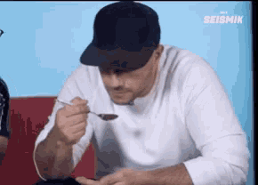 a man is eating something with a spoon and the word seismik is on the bottom right