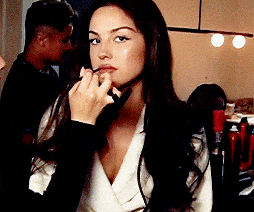a woman with long dark hair is applying makeup to her lips