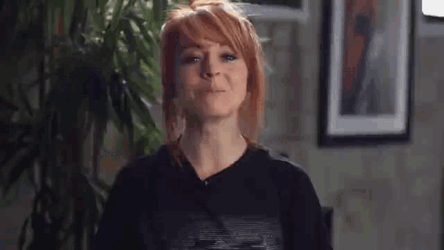 a woman with red hair is wearing a black t-shirt and making a face .