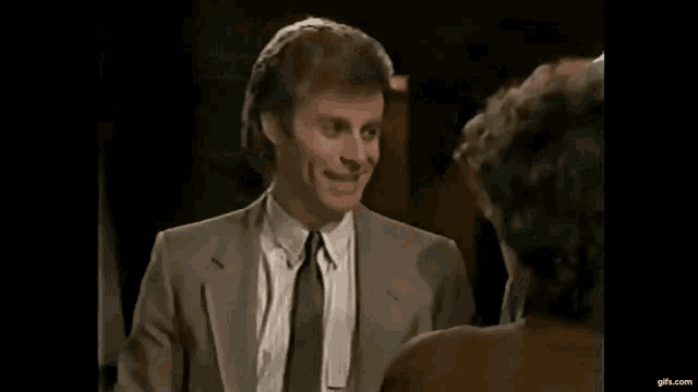 a man in a suit and tie is smiling at a woman in a brown shirt .