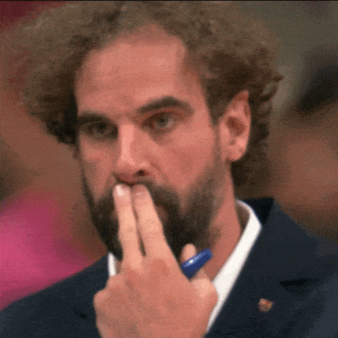 a man with curly hair and a beard is covering his mouth with his hand