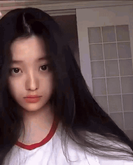 a young girl with long black hair is wearing a white shirt with a red collar .