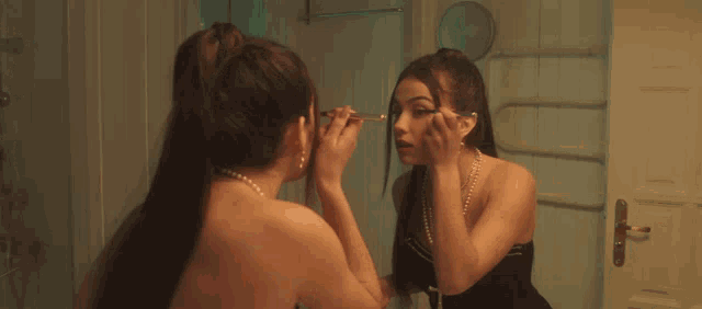 a woman applying makeup in front of a mirror with a cross on her neck
