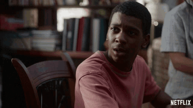 a man in a pink shirt is sitting in a chair with a netflix logo behind him