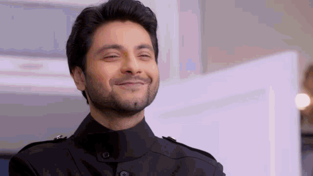 a man with a beard is smiling and wearing a black suit