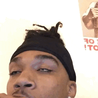 a man wearing a black headband with dreadlocks in his hair is making a funny face .