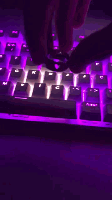 a person is typing on a keyboard that has purple lights on it