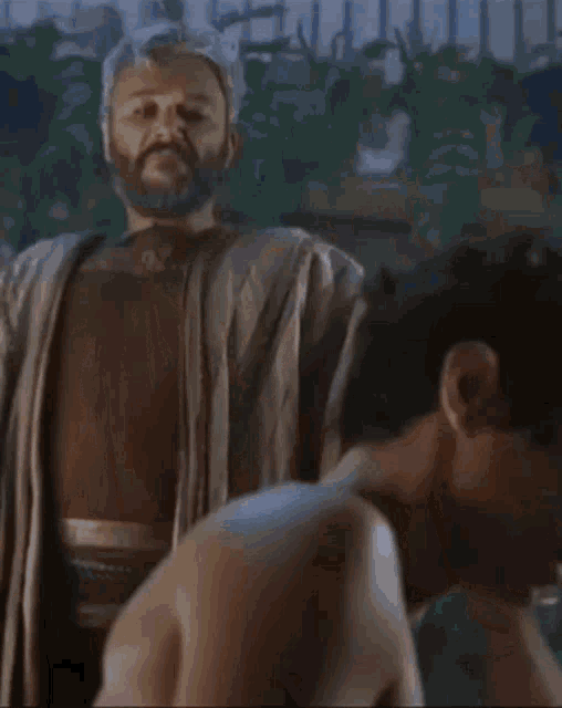 a man with a beard is standing next to a man without a shirt on .