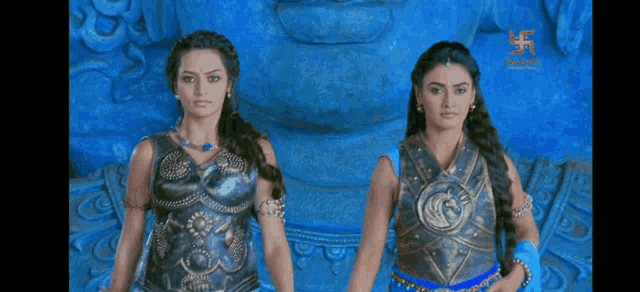 two women are standing next to each other in front of a blue statue with a swastika on it