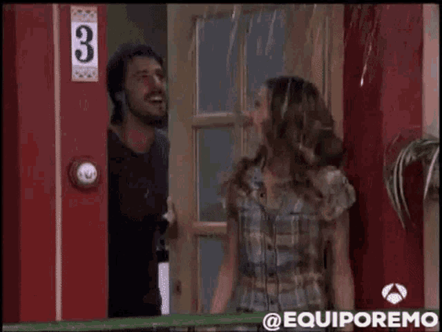 a man and a woman are standing in front of a red door with the number 3 on it