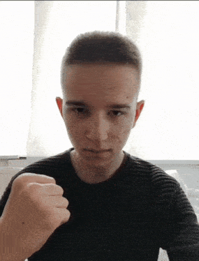 a young man wearing a black sweater is making a fist