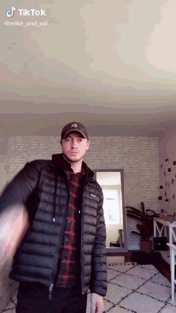 a man in a plaid shirt and a black patagonia jacket stands in a room