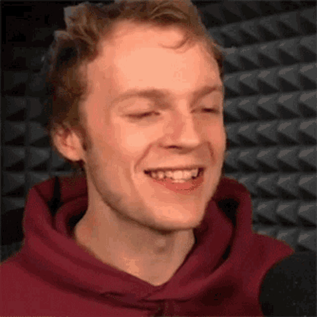 a man in a red hoodie is smiling in front of a microphone in a recording studio .