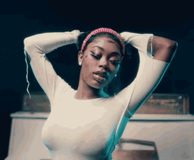 a woman wearing a headband and a white shirt holds her hands in her hair