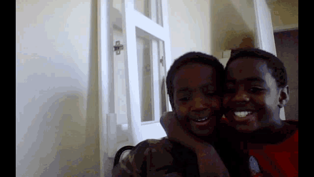 two young boys are hugging each other and smiling for a picture .