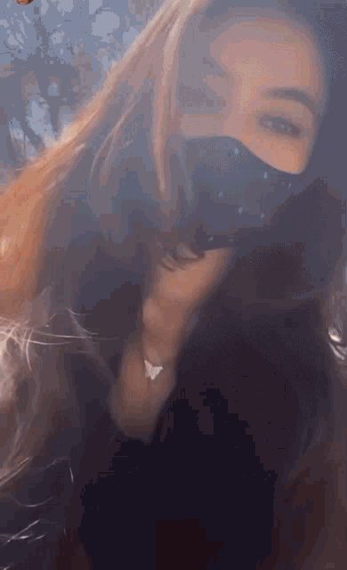a woman wearing a black face mask with a butterfly necklace