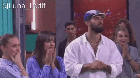 a group of people are sitting in a room with a man wearing a white shirt and a blue hat .
