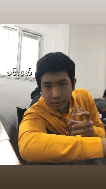 a young man in a yellow shirt is holding a glass in his hand