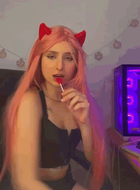 a woman with long pink hair is eating a lollipop in front of a computer case .