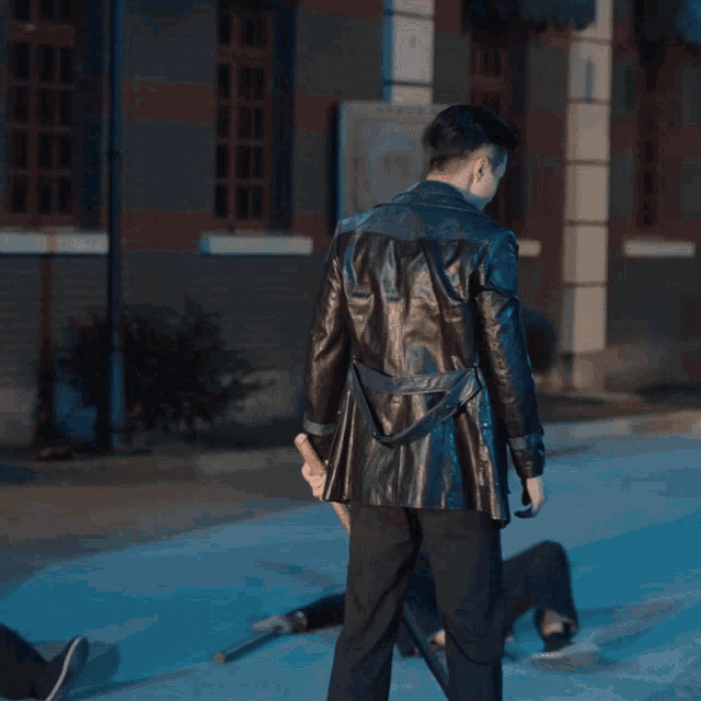 a man in a black leather jacket stands on a sidewalk