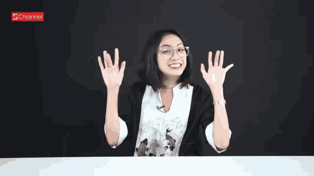 a woman sitting at a table with her hands in the air and a channel logo in the background
