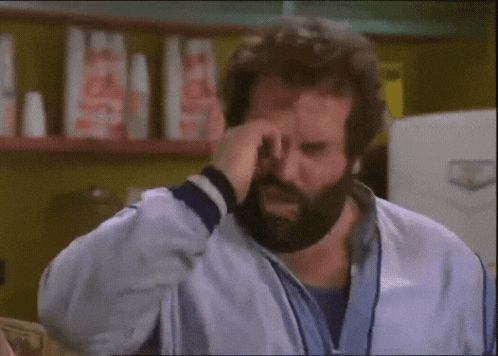 a man with a beard is covering his face with his hand in a kitchen .