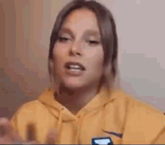 a close up of a woman wearing a yellow hoodie talking .