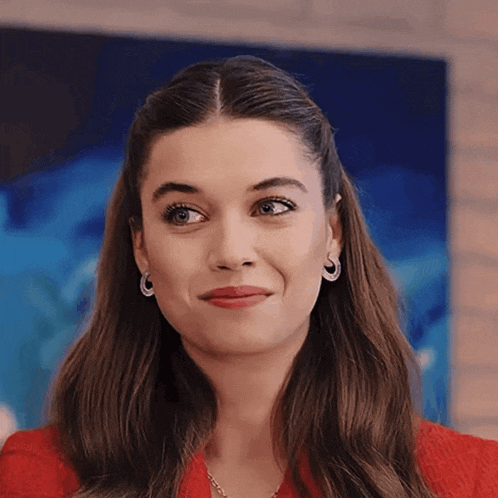 a woman wearing hoop earrings and a red jacket looks at the camera