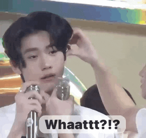 a young man is holding a microphone and making a funny face while another person adjusts his hair .
