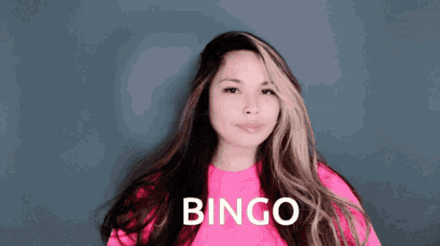 a woman in a pink sweater is making a bingo gesture