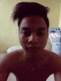 a man without a shirt is taking a selfie with his hair in a messy bun .