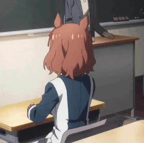a girl with red hair is sitting at a desk in a classroom with a man standing behind her .