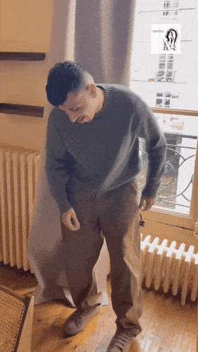 a man in a grey sweater and brown pants is standing in front of a radiator