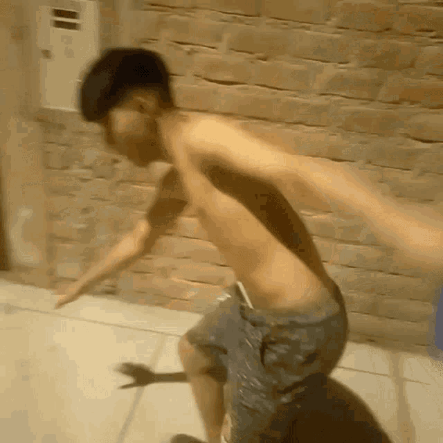a young man without a shirt is jumping in the air while standing on a sidewalk in front of a brick wall .
