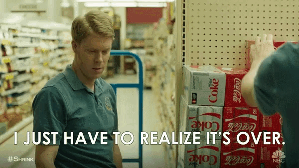 a man in a blue shirt is talking to another man in front of a stack of coke cans