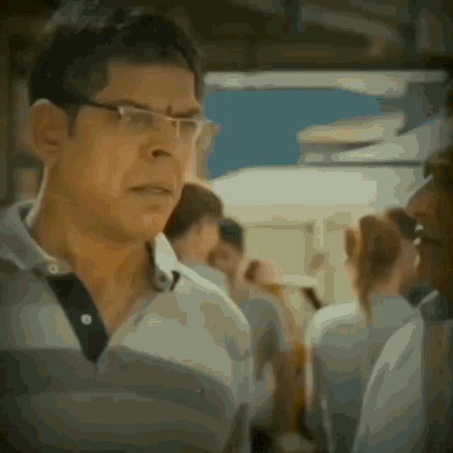 a man wearing glasses and a white shirt stands in a crowd of people