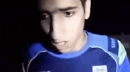 a young man in a blue shirt is standing in the dark .