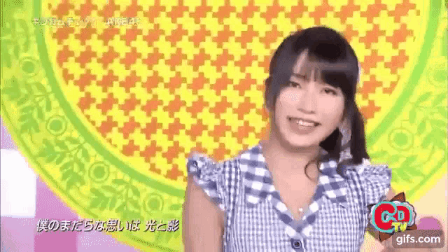 a woman in a blue and white plaid shirt is smiling in front of a yellow and green background .