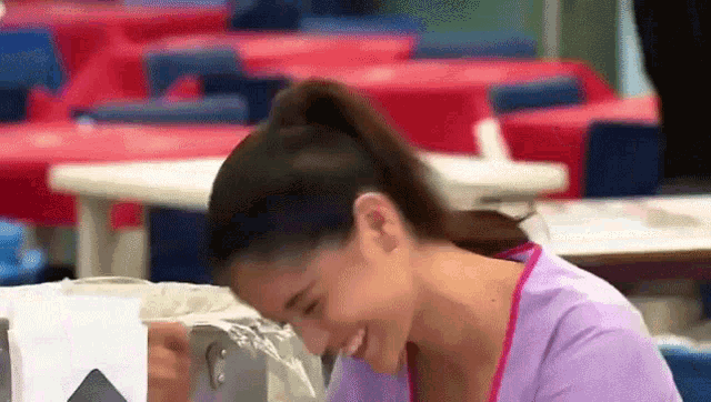 a woman in a purple shirt is smiling while sitting at a table in a cafeteria .