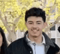 a young man in a black jacket is smiling for a picture while standing next to a woman .