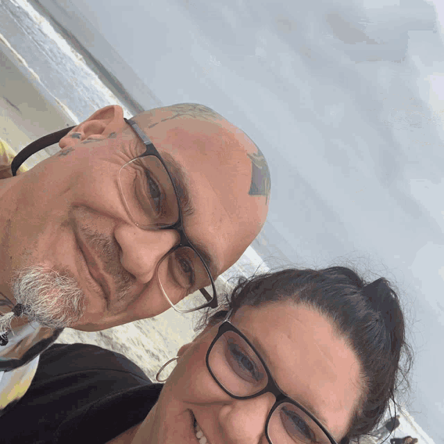 a man with glasses and a tattoo on his forehead smiles with a woman