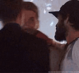 a man in a baseball cap is talking to another man in a dark room .