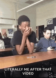 a boy is sitting at a desk in a classroom with his hands on his face .