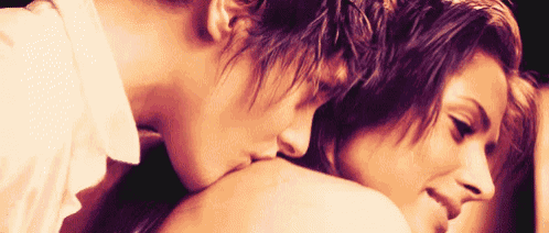 a man is kissing a woman 's shoulder and the woman is smiling