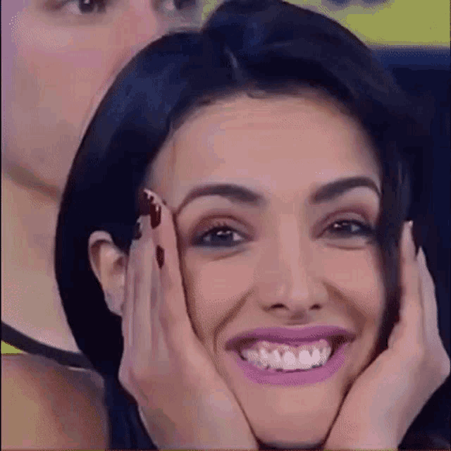 a woman is smiling with her hands on her face while a man looks on .