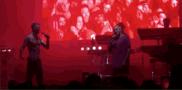 two men singing on a stage with a crowd watching