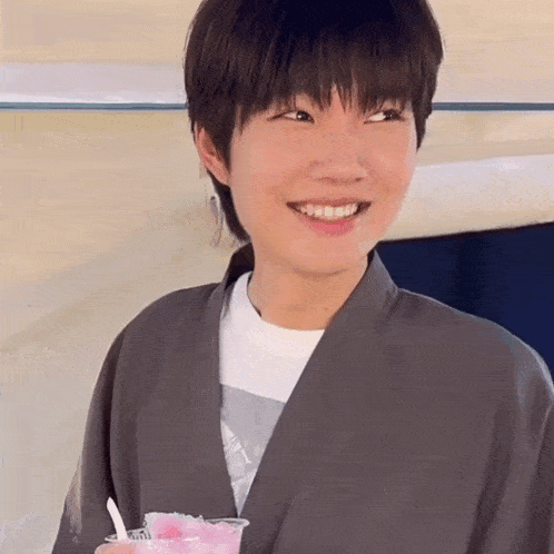 a young man in a kimono is smiling while holding a cup of pink ice cream .