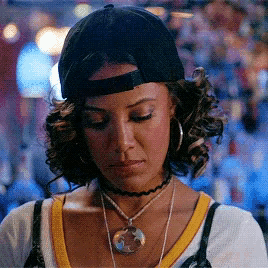 a woman wearing a baseball cap and choker necklace looks down