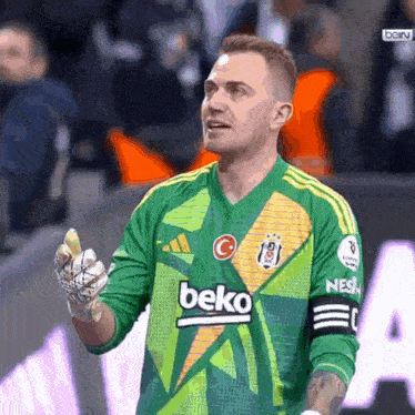 a soccer player wearing a green beko jersey holds up his hand