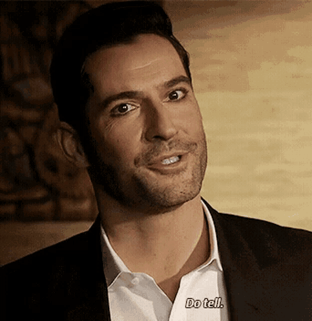 a man in a suit and white shirt is smiling and says do tell